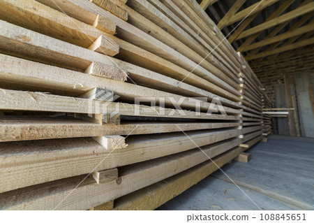 Neatly piled long stack of wooden boards inside attic room under construction. Neatly piled long stack of wooden boards inside attic room under construction. 108845651