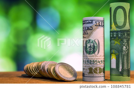 One hundred euro and one hundred US dollar rolled bills banknotes, with euro coins and american cents on green blurred bokeh background. One hundred euro and one hundred US dollar rolled bills banknotes, with euro coins and american cents on green blurred bokeh background. 108845781