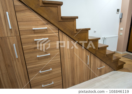 Modern architecture interior with luxury hallway with glossy wooden stairs in multi-storey house. Custom built pullout cabinets on glides in slots under stairs. Use of space for storage. 108846119