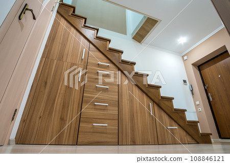 Modern architecture interior with luxury hallway with glossy wooden stairs in multi-storey house. Custom built pullout cabinets on glides in slots under stairs. Use of space for storage. 108846121