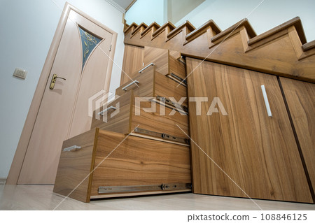 Modern architecture interior with luxury hallway with glossy wooden stairs in multi-storey house. Custom built pullout cabinets on glides in slots under stairs. Use of space for storage. 108846125