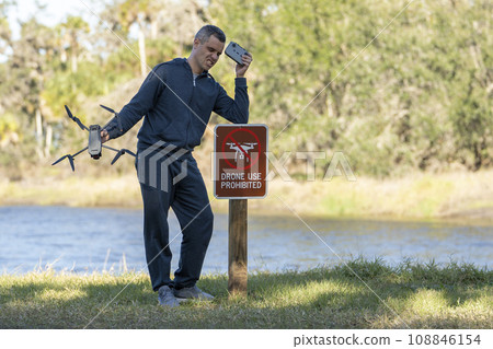 Man is sad that he is not allowed to fly his quadcopter state park no drone area. Operator is unauthorised to use UAS near restriction sign Man is sad that he is not allowed to fly his quadcopter state park no drone area. Operator is unauthorised to use UAS near restriction sign 108846154