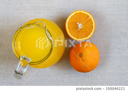 Jug and glass of orange juice and ripe oranges from above, top view on burlap sackcloth background 108846221