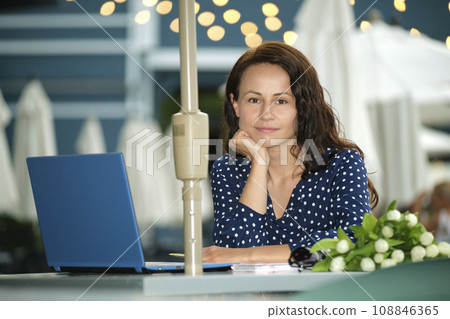 Happy young businesswoman sitting at outdoor cafe table working remotely on laptop computer. Making business online concept Happy young businesswoman sitting at outdoor cafe table working remotely on laptop computer. Making business online concept 108846365
