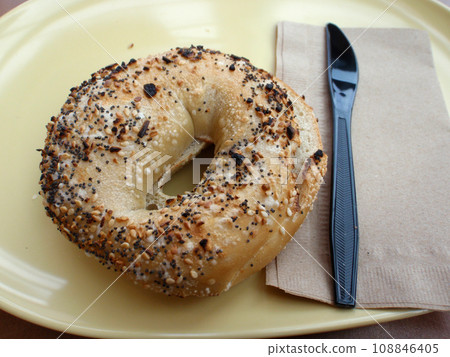 Everything Bagel and Plastic Knife on a yellow plate 108846405