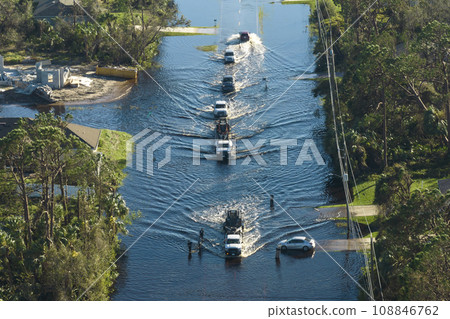 Flooded American street with moving vehicles and surrounded with water houses in Florida residential area. Consequences of hurricane natural disaster 108846762