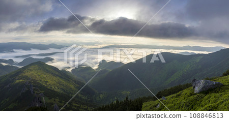 Fantastic view of mountain valley covered with low white puffy like snow clouds stretching to foggy horizon under bright morning sky with light orange glow at sunrise. Beauty of nature concept. Fantastic view of mountain valley covered with low white puffy like snow clouds stretching to foggy horizon under bright morning sky with light orange glow at sunrise. Beauty of nature concept. 108846813