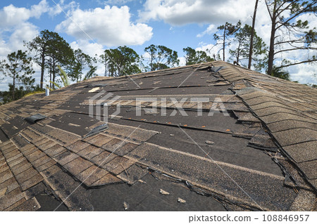 Damaged house roof with missing shingles after hurricane Ian in Florida. Consequences of natural disaster Damaged house roof with missing shingles after hurricane Ian in Florida. Consequences of natural disaster 108846957