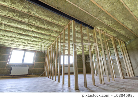 Construction and renovation of big light spacious empty room with oak floor, walls and ceiling insulated with rock wool, heating radiators under low attic windows and wooden frame for future walls. 108846983