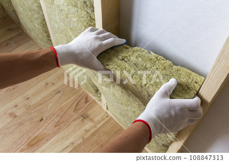 Close-up of worker hands in white gloves insulating rock wool insulation staff in wooden frame for future walls for cold barrier. Comfortable warm home, economy, construction and renovation concept. 108847313