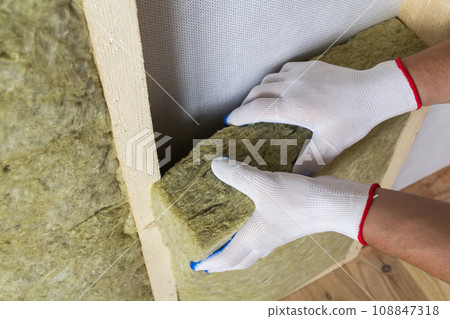 Close-up of worker hands in white gloves insulating rock wool insulation staff in wooden frame for future walls for cold barrier. Comfortable warm home, economy, construction and renovation concept. 108847318