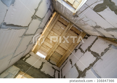 Close-up detail of house room interior under construction and renovation. Energy saving walls of hollow foam insulation blocks, wooden ceiling beams for roof frame. Close-up detail of house room interior under construction and renovation. Energy saving walls of hollow foam insulation blocks, wooden ceiling beams for roof frame. 108847366