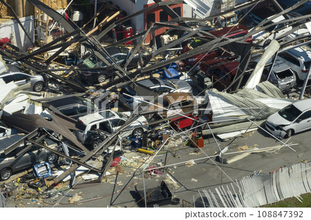 Car dealership building destroyed by hurricane with damaged cars under ruins in Florida. Natural disaster and its consequences 108847392