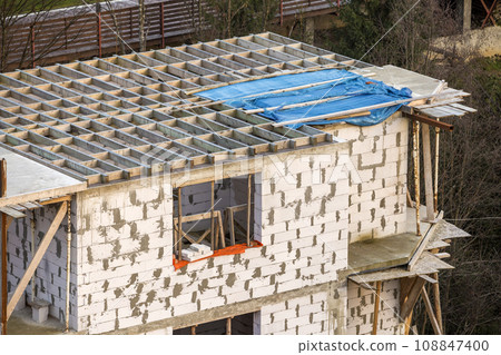 Building under construction. Roof beams frame and roofing underlayment, water-resistant waterproof barrier on walls of hollow foam insulation blocks. Masonry, roofing and renovation. 108847400