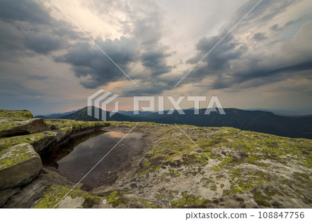 Blue sky reflected in small lake on rocky mountain peak on blue mountain range background at dawn. 108847756