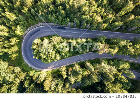 Aerial view of winding road in high mountain pass trough dense green pine woods. 108847835