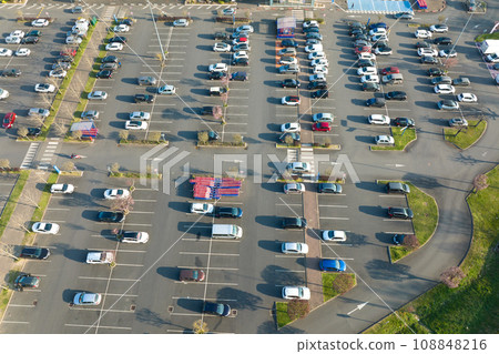Aerial view of many colorful cars parked on parking lot with lines and markings for parking places and directions Aerial view of many colorful cars parked on parking lot with lines and markings for parking places and directions 108848216