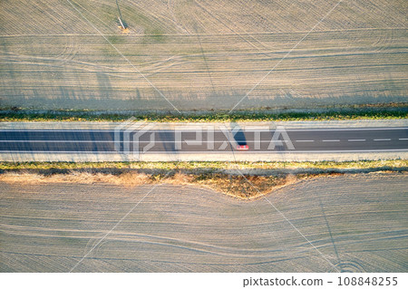 Aerial view of intercity road with blurred fast driving car at sunset. Top view from drone of highway traffic in evening Aerial view of intercity road with blurred fast driving car at sunset. Top view from drone of highway traffic in evening 108848255