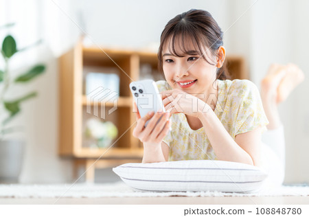 A woman who operates a smartphone in the living room. 108848780