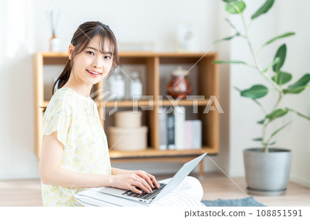 A woman operating a laptop in the living room. 108851591