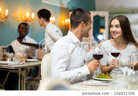 Couple drinking red wine in restaurant and talking Couple drinking red wine in restaurant and talking 108852506