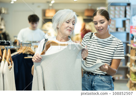Young girl consults senior female friend about purchasing sweater during shopping Young girl consults senior female friend about purchasing sweater during shopping 108852507