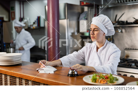 Female cook reads the paid check and presses the bell for the waiter in restaurant 108852564