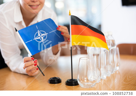 Little flag of Germany on table and flag of NATO put next to it by young woman 108852738