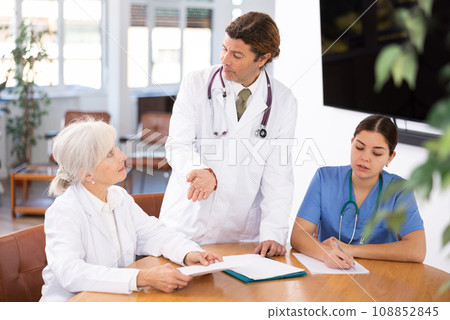 Group of professional doctors sitting at table and discussing diagnosis and treatment of patients during medical council Group of professional doctors sitting at table and discussing diagnosis and treatment of patients during medical council 108852845
