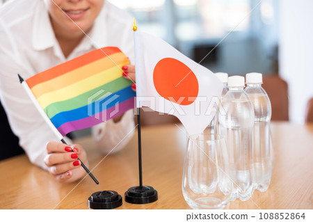 Little flag of Japan on table and LGBT flag put next to it by young woman 108852864