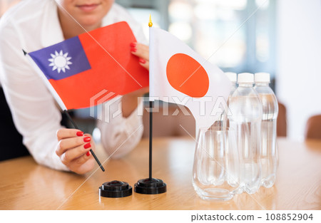 Female hands placing flags of Taiwan and Japan on table before meeting 108852904