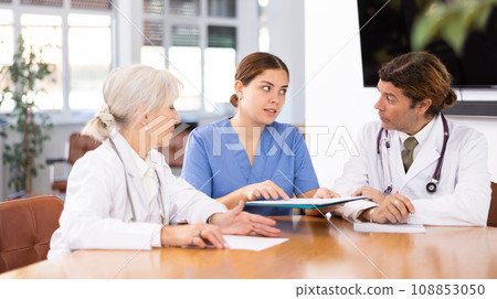 Group of professional doctors sitting at table and discussing diagnosis and treatment of patients during medical council Group of professional doctors sitting at table and discussing diagnosis and treatment of patients during medical council 108853050