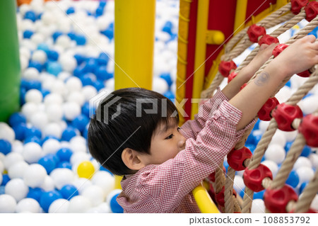 A little boy practices climbing a rope net in the play park. A little boy practices climbing a rope net in the play park. 108853792