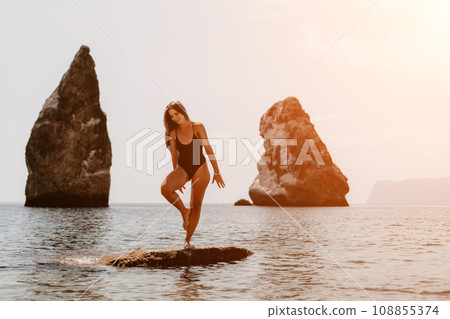 Woman sea yoga. Back view of free calm happy satisfied woman with long hair standing on top rock with yoga position against of sky by the sea. Healthy lifestyle outdoors in nature, fitness concept. 108855374