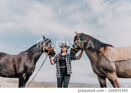 Young happy woman in hat with her horse in evening sunset light. Outdoor photography with fashion model girl. Lifestyle mood. Concept of outdoor riding, sports and recreation. 108855395