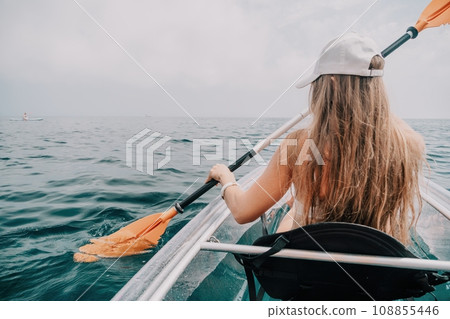 Woman in kayak back view. Happy young woman with long hair floating in transparent kayak on the crystal clear sea. Summer holiday vacation and cheerful female people relaxing having fun on the boat Woman in kayak back view. Happy young woman with long hair floating in transparent kayak on the crystal clear sea. Summer holiday vacation and cheerful female people relaxing having fun on the boat 108855446