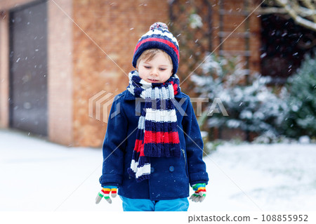 Cute little funny child in colorful winter fashion clothes having fun and playing with snow, outdoors during snowfall. Active outdoors leisure with children. Kid boy and toddler catching snowflakes. 108855952