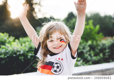 Little blond preschool girl watching soccer football cup game on public viewing. Happy joyful excited child about winning game match of favorite national football team. girl with German flag on face. 108856081