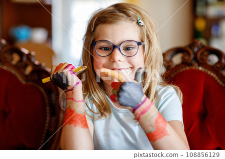Little preschool girl painting with felt pens on hands. Creative cute child showing hands and arms painted with colorful pens or water colors. Laughing happy kid. 108856129