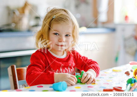 Adorable cute little toddler girl with colorful clay. Healthy baby playing and creating toys from play dough. Small kid molding modeling clay and learning 108856151