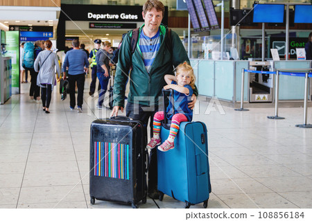 Cute little toddler girl and father at the airport. Happy family traveling by plane, making vacations. Young dad and baby daughter with suitcases waiting for flight. Family going on journey. Ireland Cute little toddler girl and father at the airport. Happy family traveling by plane, making vacations. Young dad and baby daughter with suitcases waiting for flight. Family going on journey. Ireland 108856184