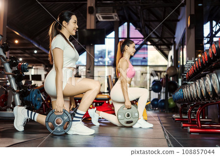 Two young asian woman doing exercises with heavy weights plates in gym. 108857044