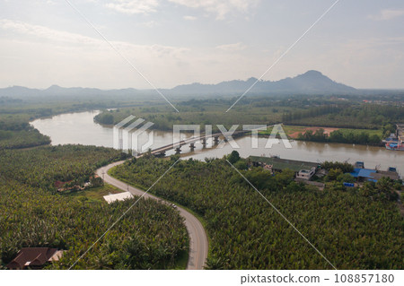 Aerial top view of a bridge with garden park with green mangrove forest trees, river, pond or lake. Nature landscape background, Thailand. Aerial top view of a bridge with garden park with green mangrove forest trees, river, pond or lake. Nature landscape background, Thailand. 108857180