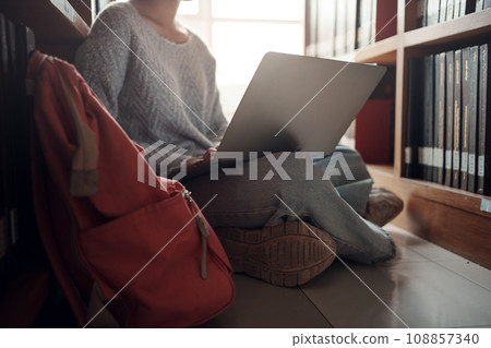 Student girl sitting on floor and using laptop, Writes notes for paper, Essay, Study for class assignment. Diverse group of Students Learning, Studying for Exams. Student girl sitting on floor and using laptop, Writes notes for paper, Essay, Study for class assignment. Diverse group of Students Learning, Studying for Exams. 108857340
