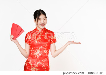 Asian woman wearing traditional cheongsam qipao dress showing something and holding angpao or red packet monetary gift isolated on white background. Happy Chinese new year. Asian woman wearing traditional cheongsam qipao dress showing something and holding angpao or red packet monetary gift isolated on white background. Happy Chinese new year. 108858105