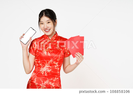 Asian woman wearing traditional cheongsam qipao dress holding smartphone and holding angpao or red packet monetary gift isolated on white background.Happy Chinese new year. Asian woman wearing traditional cheongsam qipao dress holding smartphone and holding angpao or red packet monetary gift isolated on white background.Happy Chinese new year. 108858106