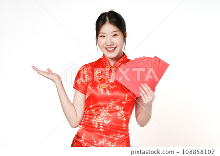 Asian woman wearing traditional cheongsam qipao dress showing something and holding angpao or red packet monetary gift isolated on white background. Happy Chinese new year. Asian woman wearing traditional cheongsam qipao dress showing something and holding angpao or red packet monetary gift isolated on white background. Happy Chinese new year. 108858107