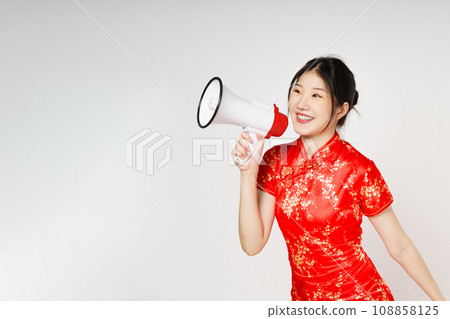Asian woman wearing traditional cheongsam qipao dress with gesture holding megaphone isolated on white background. Happy Chinese new year. Asian woman wearing traditional cheongsam qipao dress with gesture holding megaphone isolated on white background. Happy Chinese new year. 108858125