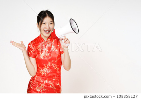 Asian woman wearing traditional cheongsam qipao dress with gesture holding megaphone isolated on white background. Happy Chinese new year. Asian woman wearing traditional cheongsam qipao dress with gesture holding megaphone isolated on white background. Happy Chinese new year. 108858127