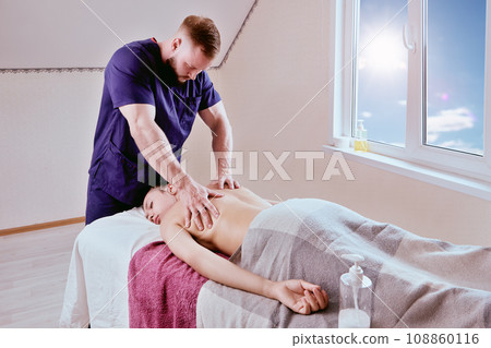Woman in her 20s lies on massage table while masseur kneads her back muscles. 108860116